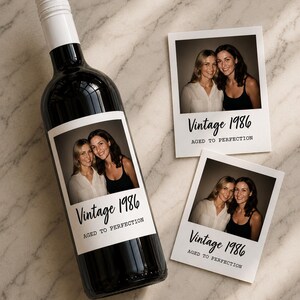 May include: A dark glass wine bottle with a white screw cap and a custom label featuring a photograph of two people, the text Vintage 1986, and the phrase AGED TO PERFECTION. Two matching rectangular photo prints are placed next to the bottle.
