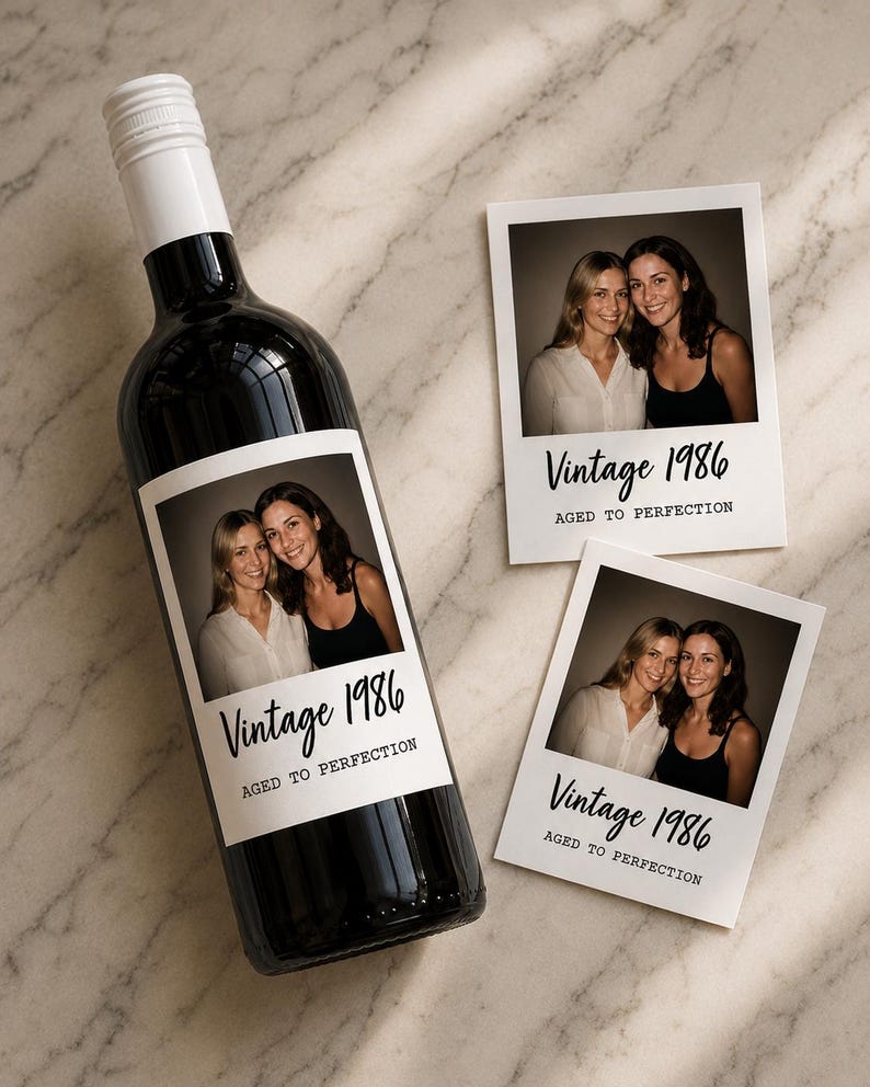 May include: A dark glass wine bottle with a white screw cap and a custom label featuring a photograph of two people, the text Vintage 1986, and the phrase AGED TO PERFECTION. Two matching rectangular photo prints are placed next to the bottle.