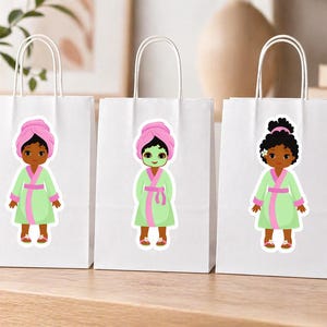 May include: Three white gift bags with spa-themed stickers. Each sticker features a cartoon figure wearing a pink towel, a green robe with pink trim, and a spa treatment. The bags have white handles and are arranged on a light-colored surface.