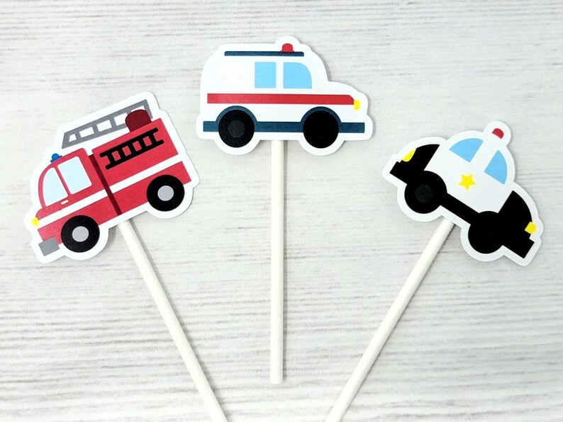 May include: Set of three vehicle-themed cupcake toppers. Includes a red fire truck, a white ambulance with red stripes, and a black and white police car with a yellow star. Each topper is attached to a white stick.