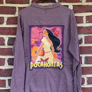 May include: Purple and white plaid long-sleeved shirt with a large, colorful patch on the back featuring a cartoon image of Pocahontas with the text "Pocahontas" underneath.