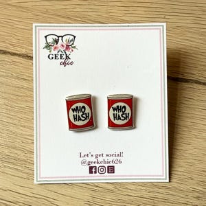 May include: A pair of novelty earrings featuring a red can design with the text "WHO HASH" in white. The earrings are displayed on a white card with the "Geek Chic" logo and social media information.
