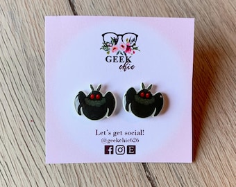 May include: A pair of black and white earrings with a red-eyed creature design. The earrings are on a white card with the text "GEEK chic" and "Let's get social! @geekchic626"