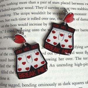 May include: A pair of novelty earrings featuring a white underwear design with red heart accents and the text "YOU WILL NOT BREAK ME!". The earrings also have a red heart-shaped top.