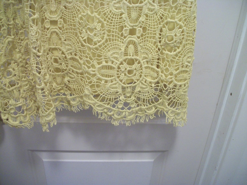 Puede incluir: Primer plano de una tela de encaje amarillo p&aacute;lido. El encaje presenta un intrincado dise&ntilde;o floral con un borde festoneado. La tela parece ser parte de una prenda, posiblemente un vestido o una blusa.