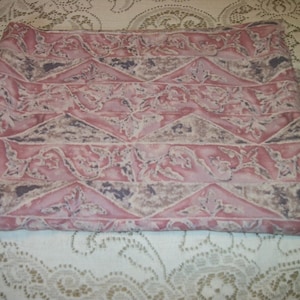 May include: Folded fabric featuring a repeating pattern of pink, grey, and brown geometric shapes and floral designs. The fabric appears to be a cotton or linen blend, suitable for sewing or home decor.