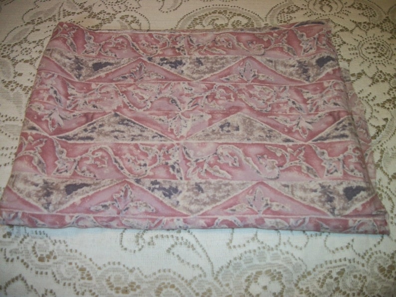 May include: Folded fabric featuring a repeating pattern of pink, grey, and brown geometric shapes and floral designs. The fabric appears to be a cotton or linen blend, suitable for sewing or home decor.