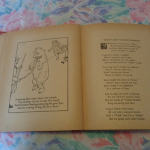 May include: Open book with illustrations and text. One page shows a dancing bear illustration with text below. The opposite page has a poem titled "Dixie and Yankee Doodle". The book has a red spine and aged pages.
