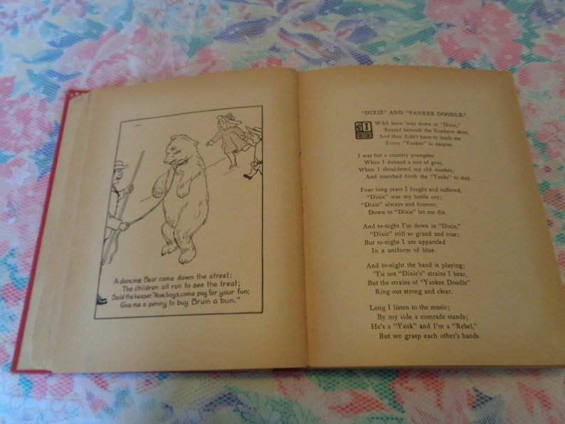 May include: Open book with illustrations and text. One page shows a dancing bear illustration with text below. The opposite page has a poem titled "Dixie and Yankee Doodle". The book has a red spine and aged pages.