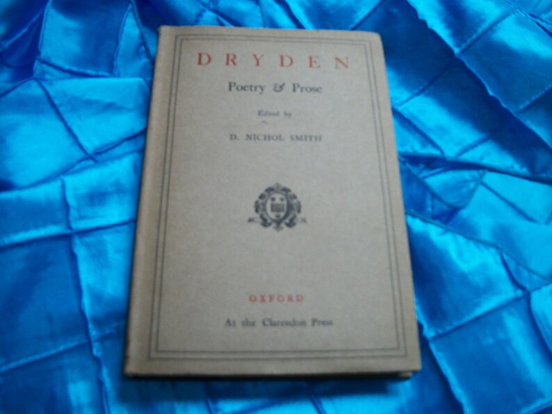 May include: A vintage book titled "Dryden Poetry & Prose" with a beige cover and red lettering. The book is edited by D. Nichol Smith and published by Oxford at the Clarendon Press. The book is on a blue fabric surface.