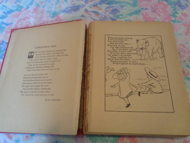 May include: Open vintage book with red cover. The left page features the poem "Christmas Day" by Susan Coolidge. The right page has an illustration of an elephant and children with a poem. The book's pages are aged.