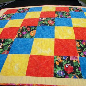 May include: A colorful quilt with a checkerboard pattern. The quilt features alternating squares of red, yellow, and blue. Some squares have a black background with a fish and coral pattern. The quilt has a yellow border.
