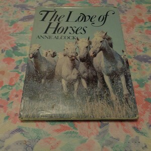 May include: A book titled "The Love of Horses" by Anne Alcock. The cover shows a painting of white horses galloping through water. The title is in a decorative font against a light blue backdrop.