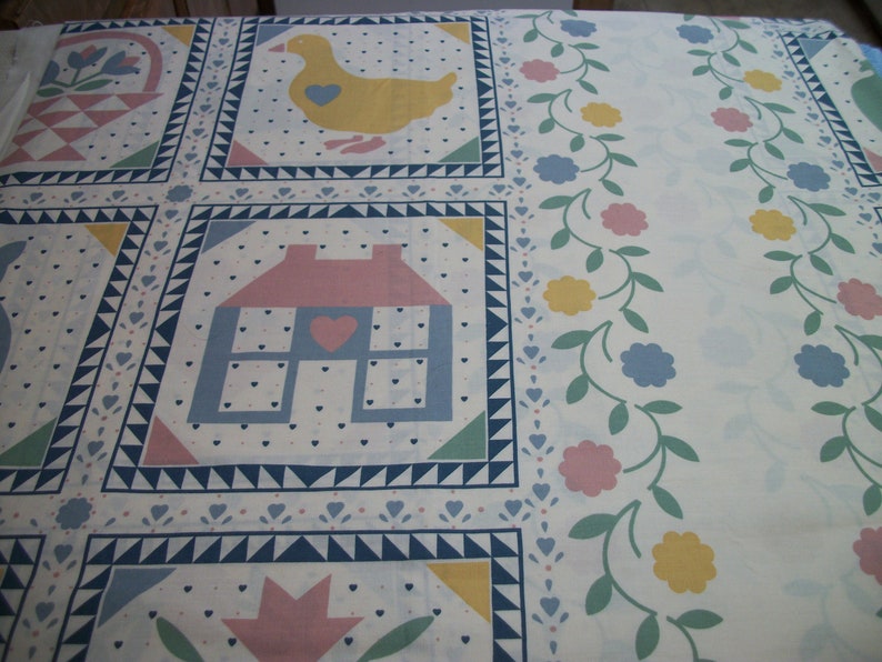 May include: A white fabric with a repeating pattern of squares featuring a house, duck, and floral basket. The design includes blue, pink, yellow, and green accents, with a border of flowers and vines.