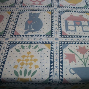 May include: A white quilt with a repeating pattern of squares. Each square features a different design, including a cat with a heart, a house, and flowers. The quilt has a border of blue triangles and hearts, with a soft, pastel color palette.