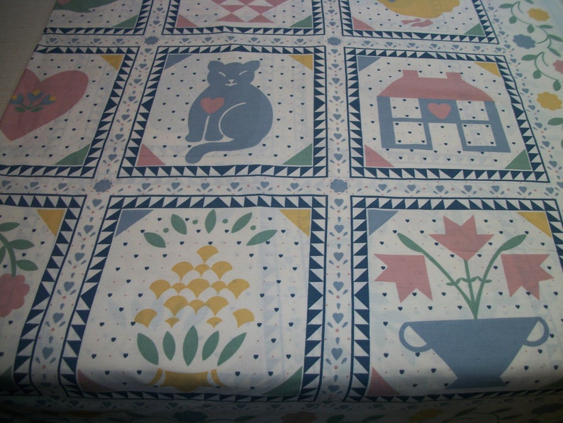 May include: A white quilt with a repeating pattern of squares. Each square features a different design, including a cat with a heart, a house, and flowers. The quilt has a border of blue triangles and hearts, with a soft, pastel color palette.