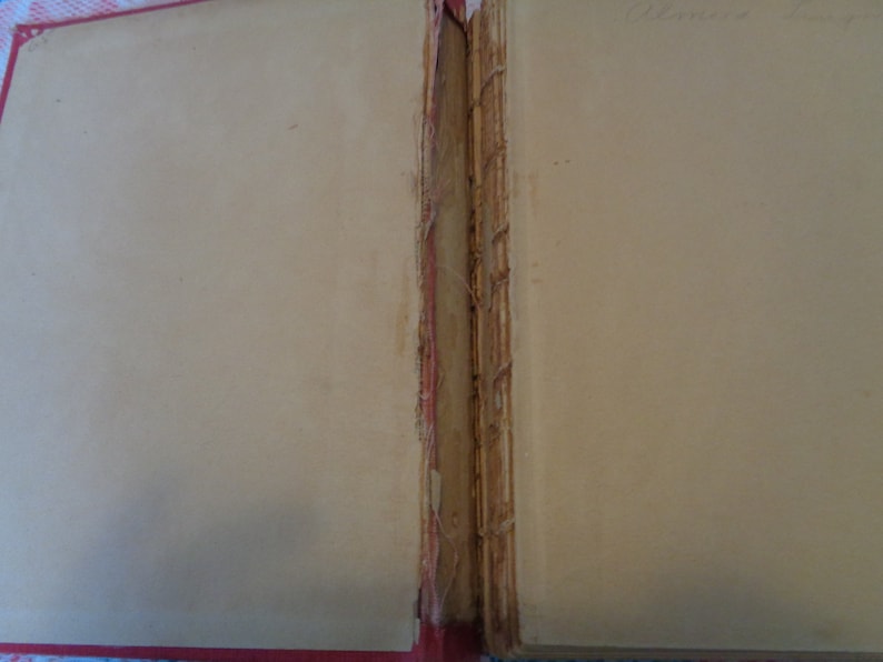 May include: Open view of an antique book with aged, cream-colored pages. The binding is visible, showing the spine's construction with visible threads and a red border. The text "Delores Long" is handwritten in the upper right corner.
