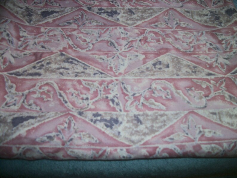 May include: Close-up of a fabric featuring a repeating pattern in pink, beige, and dark grey. The design incorporates triangles and floral motifs, giving a textured appearance. The fabric has a soft, faded aesthetic.