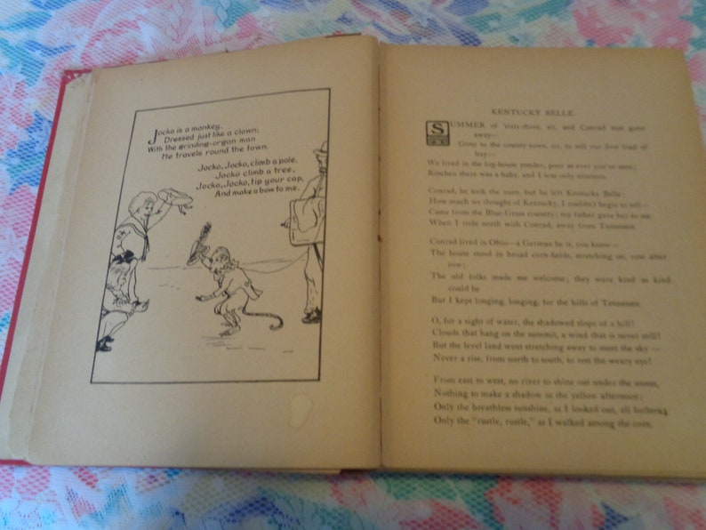 May include: An open vintage book with red binding, displaying two pages. The left page features a black and white illustration of a monkey and a boy, with accompanying text. The right page contains printed text titled "Kentucky Belle".