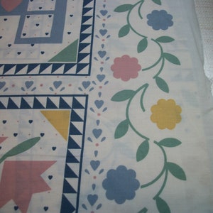 May include: White fabric with a patchwork design featuring blue, pink, and yellow floral and geometric patterns. The border has a floral vine design with pink, yellow, and blue flowers and green leaves. The fabric has a light blue and white color scheme.