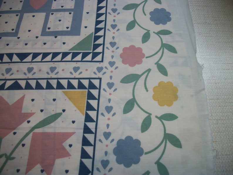 May include: White fabric with a patchwork design featuring blue, pink, and yellow floral and geometric patterns. The border has a floral vine design with pink, yellow, and blue flowers and green leaves. The fabric has a light blue and white color scheme.