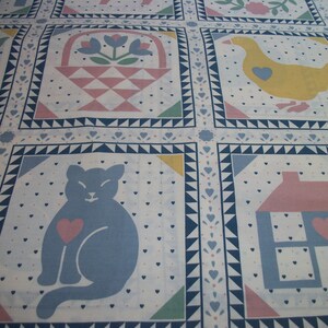May include: A white fabric with a repeating pattern of squares, each containing a different image. The images include a blue cat with a pink heart, a yellow duck with a blue heart, and a pink house with a blue heart.