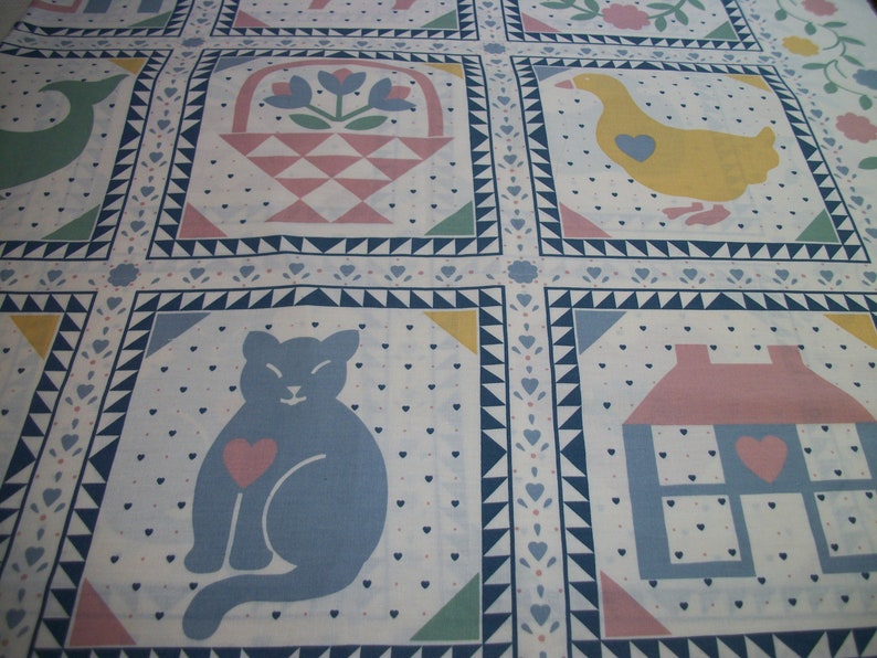 May include: A white fabric with a repeating pattern of squares, each containing a different image. The images include a blue cat with a pink heart, a yellow duck with a blue heart, and a pink house with a blue heart.