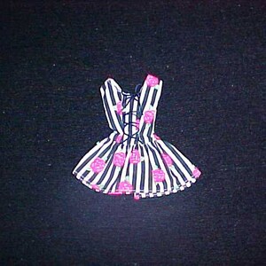 May include: A doll-sized dress with a black and white striped pattern, accented with pink floral designs. The dress features a laced back and a flared skirt, creating a playful and feminine look. The overall design is a mix of stripes and floral elements.