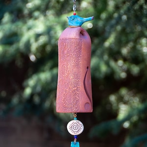 May include: A terracotta wind chime with a blue bird at the top, a white ceramic bead with a spiral design, and a blue glass teardrop-shaped pendant.
