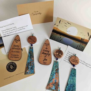 May include: Memorial wind chimes featuring wooden teardrop and circular plaques engraved with names, dates, and tree motifs. The chimes include textured, oxidized copper-toned metal panels, small blue beads, and accompanying sympathy cards with printed messages.