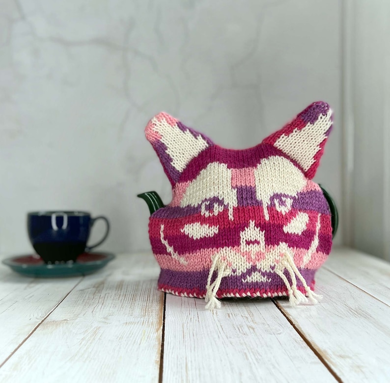 A knitted cat tea cosy with a cup and saucer