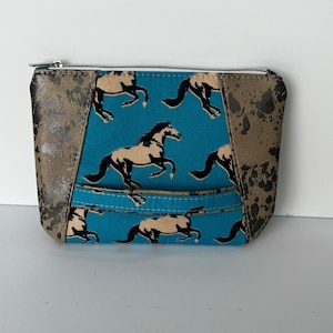 May include: A small turquoise zippered pouch with a brown and black horse print. The pouch has brown leather accents on the sides.