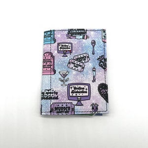 May include: A purple and blue glitter wallet with a repeating pattern of crime-themed illustrations. The illustrations include a computer screen with the text "Online Detective", a cocktail glass, a tombstone, and tickets that say "Murder" and "True Crime".