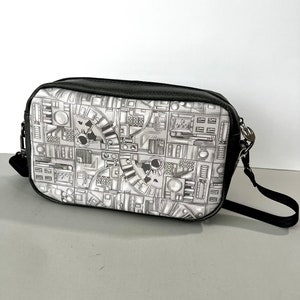 May include: A black and white crossbody bag with a graphic print of a spaceship. The bag has a black strap and a zip closure.