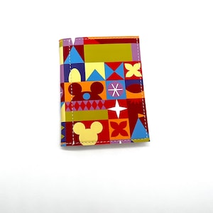 May include: A colorful passport holder with a patchwork design featuring Mickey Mouse icons. The holder is made of a durable material and has a stitched edge.