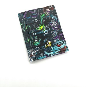 May include: A black wallet with a colorful print of cartoon characters from The Little Mermaid. The characters include Ariel, Ursula, Flounder, and Sebastian.
