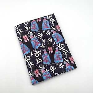 May include: A black notebook cover with a repeating pattern of a girl holding a bag of fish, with the text "XO" and skull and crossbones.