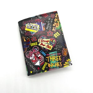 May include: Black wallet with a colorful graphic print featuring text from the show Stranger Things, including "Mouth Breather", "I Dump Your Ass", "Three Inches", and "Totally Tubular".