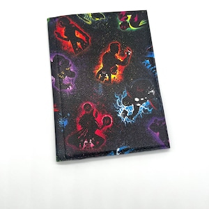 May include: Black passport holder with a colorful print of superhero silhouettes. The print features a galaxy background with stars and nebulae.