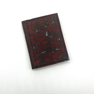 May include: A small, red leather wallet with a geometric pattern. The wallet has a black stitching detail around the edges.