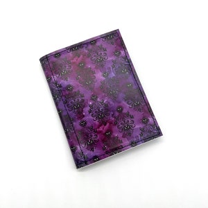 May include: A purple and black patterned notebook with a stitched edge. The pattern features a repeating design of a haunted mansion with ghosts.