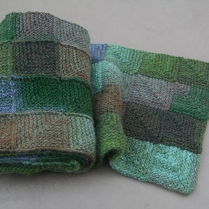 Puede incluir: Una bufanda de punto verde, marrón y azul con un diseño de patchwork.