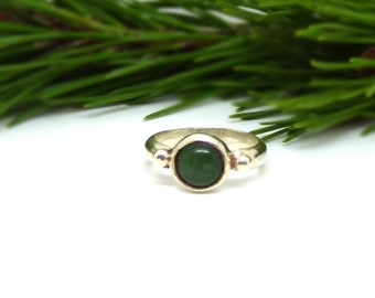 May include: A silver ring with a green oval gemstone set in the centre. The ring is surrounded by small silver beads.