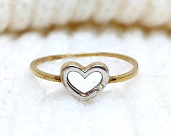 May include: A gold ring with a silver heart-shaped design. The ring is on a white fuzzy surface.