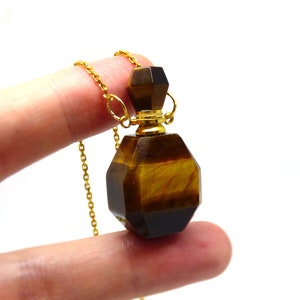 Puede incluir: Collar de cadena dorada con un colgante de frasco de perfume de ojo de tigre.