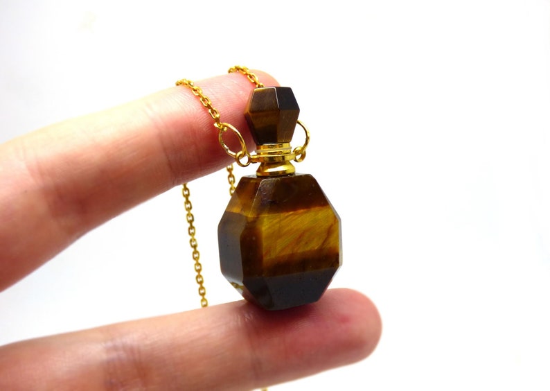 Puede incluir: Collar de cadena dorada con un colgante de frasco de perfume de ojo de tigre.