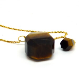 Puede incluir: Un collar de cadena dorada con dos colgantes de piedra de ojo de tigre facetados. El colgante m&aacute;s grande es de forma hexagonal y el colgante m&aacute;s peque&ntilde;o es de forma hexagonal m&aacute;s peque&ntilde;a.