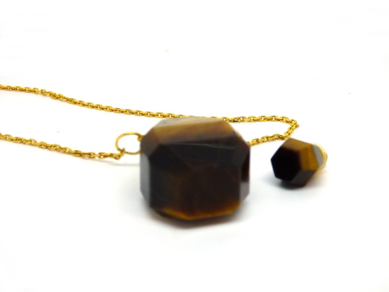 Puede incluir: Un collar de cadena dorada con dos colgantes de piedra de ojo de tigre facetados. El colgante m&aacute;s grande es de forma hexagonal y el colgante m&aacute;s peque&ntilde;o es de forma hexagonal m&aacute;s peque&ntilde;a.