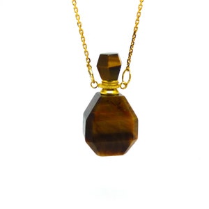 Puede incluir: Un collar de cadena dorada con un colgante de ojo de tigre marr&oacute;n y dorado en forma de botella.