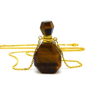 Puede incluir: Un collar de cadena dorada con un colgante de botella de piedra de ojo de tigre. La botella es facetada y tiene una tapa dorada.